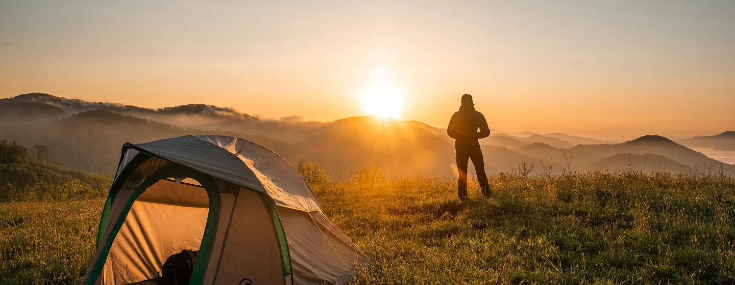 A person sits on a rock, gazing out over a vast valley under a clear blue sky